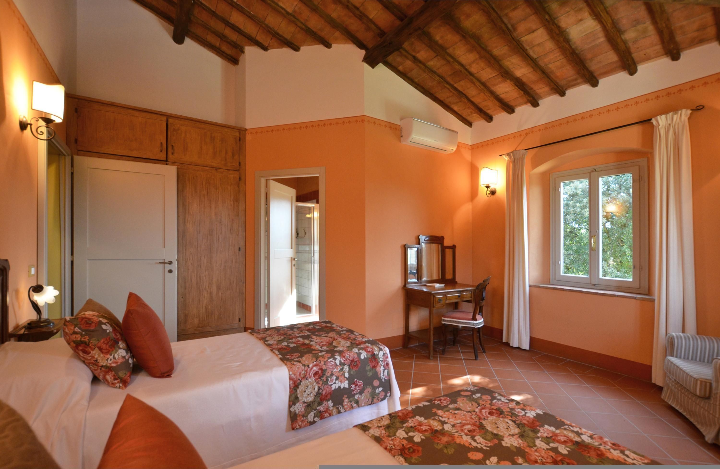 A bedroom with two beds, a desk, and a chair. There is a window with curtains and an air conditioning unit on the wall.