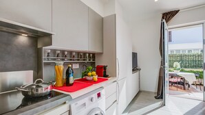 A modern kitchen with a built-in washing machine, a red countertop, and a view of the outdoor patio. - Serafina Beach House (San Bartolomeo al Mare)