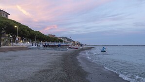 A beach with a promenade, a row of white chairs, and a small boat in the water. - Serafina Beach House (San Bartolomeo al Mare)