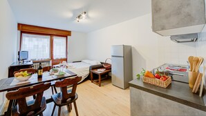 A compact kitchen with a refrigerator, a dining table with chairs, a small table with a basket, and a window with curtains. - Studio Genzianella Ski In-ski Out Mt 100 (Sestriere)