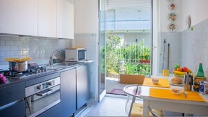 A compact kitchen with a microwave, stove, and oven, a dining area with a table and chairs, and a balcony with a view of greenery. - Spazioso App To Mare E Sport (Sanremo)