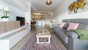 A modern living room with a grey sofa, a coffee table, and a TV on a white cabinet. There is a colorful rug and a painting of flowers on the wall. - Apartment La Cala With Pool (Mijas)