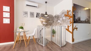 Een moderne kamer met een glazen tafel, witte stoelen, een decoratieve wand met wolkenmotieven en een lijst met een stadsgezicht.