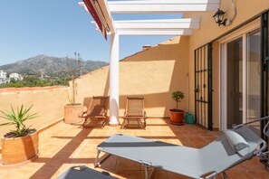 A balcony with a lounge chair, two wooden chairs, and potted plants. - Monteazul in Marbella (Marbella)