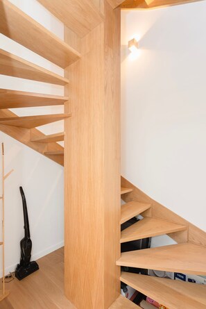 A modern wooden staircase with built-in shelves, a vacuum cleaner, and a wall-mounted light fixture. - Liiiving in Matosinhos- Colorwave Terrace House (Matosinhos)