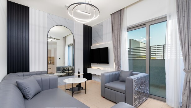 Un salon moderne avec un canapé d’angle gris, une table basse ronde et un téléviseur à écran plat fixé à un mur blanc.