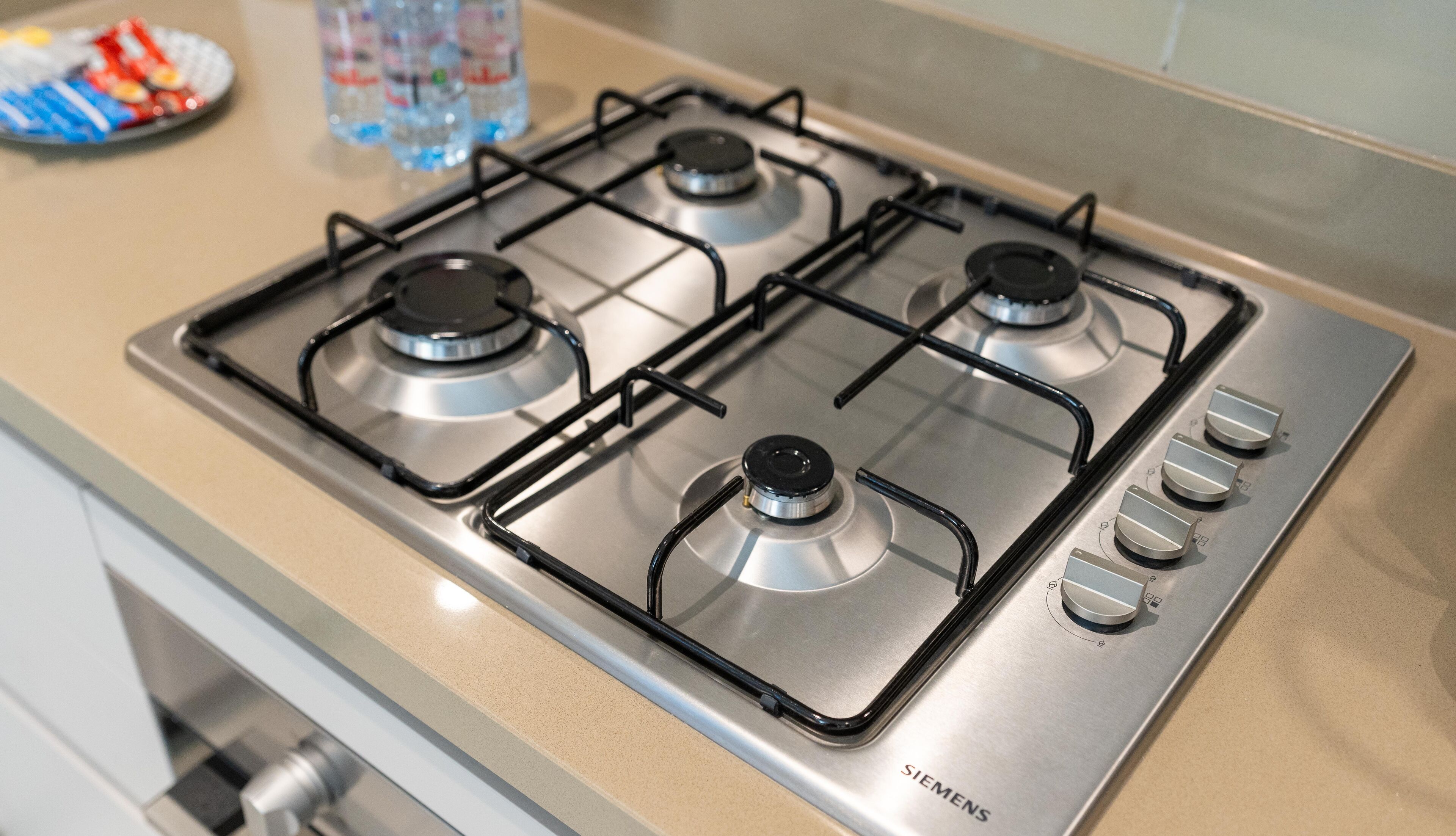 Una cocina con estufa de gas de cuatro quemadores, campana extractora de acero inoxidable y dispensador de agua en la encimera.