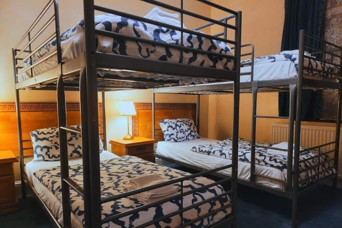 A bunk bed room with patterned bedding, a nightstand with a lamp, and a wooden headboard.