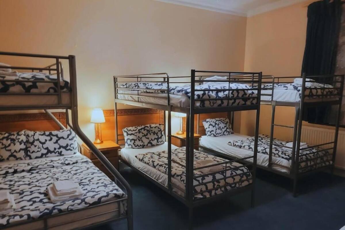 A bunk bed room with a patterned bedspread, a bedside lamp, and a window with curtains.