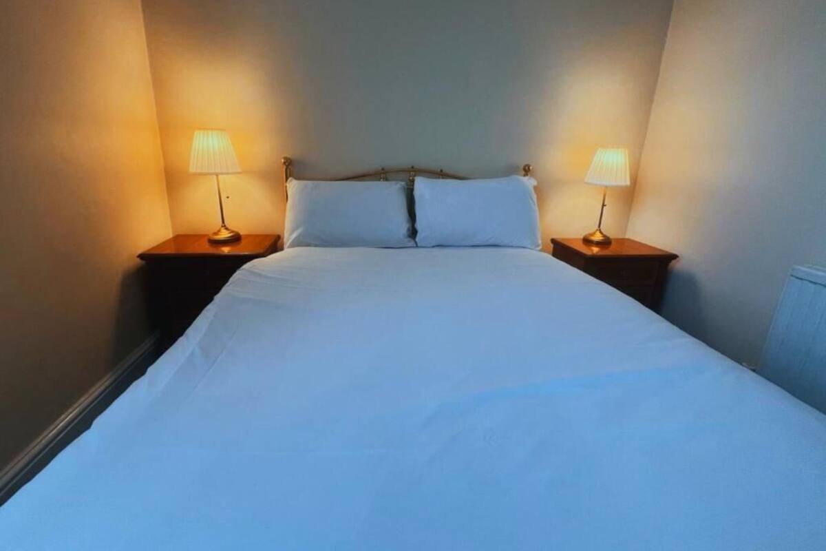 A bed with white linens, two bedside lamps, and a headboard.