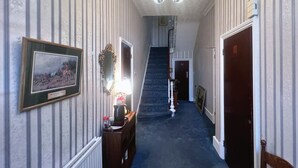 A hallway with striped wallpaper, a framed picture, a staircase, and a door. - Helen's Hotel  (London)