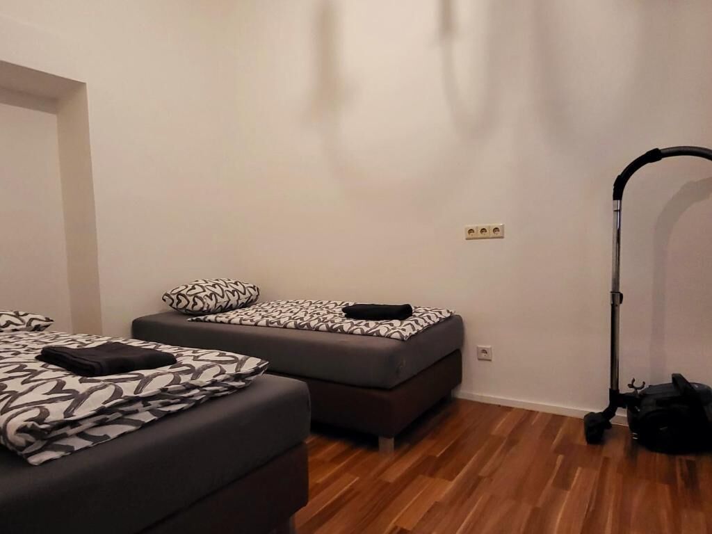 A room with two beds, a vacuum cleaner, and a power outlet on the wall.