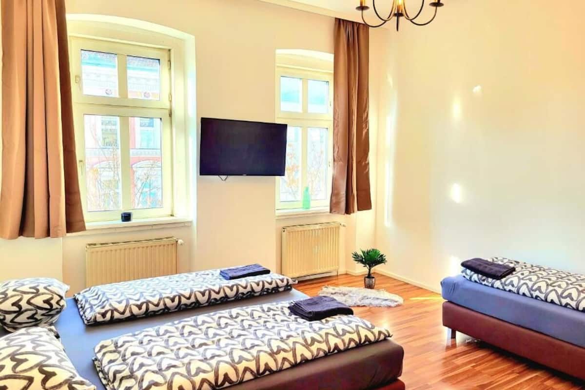 A room with two beds, a sofa, a TV, and a window with curtains.