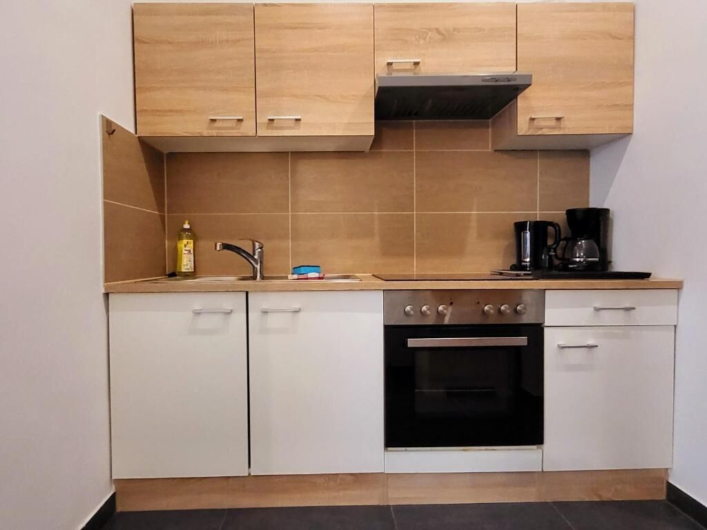 A compact kitchen with light wooden cabinets, a stainless steel oven, and a coffee maker on the countertop.
