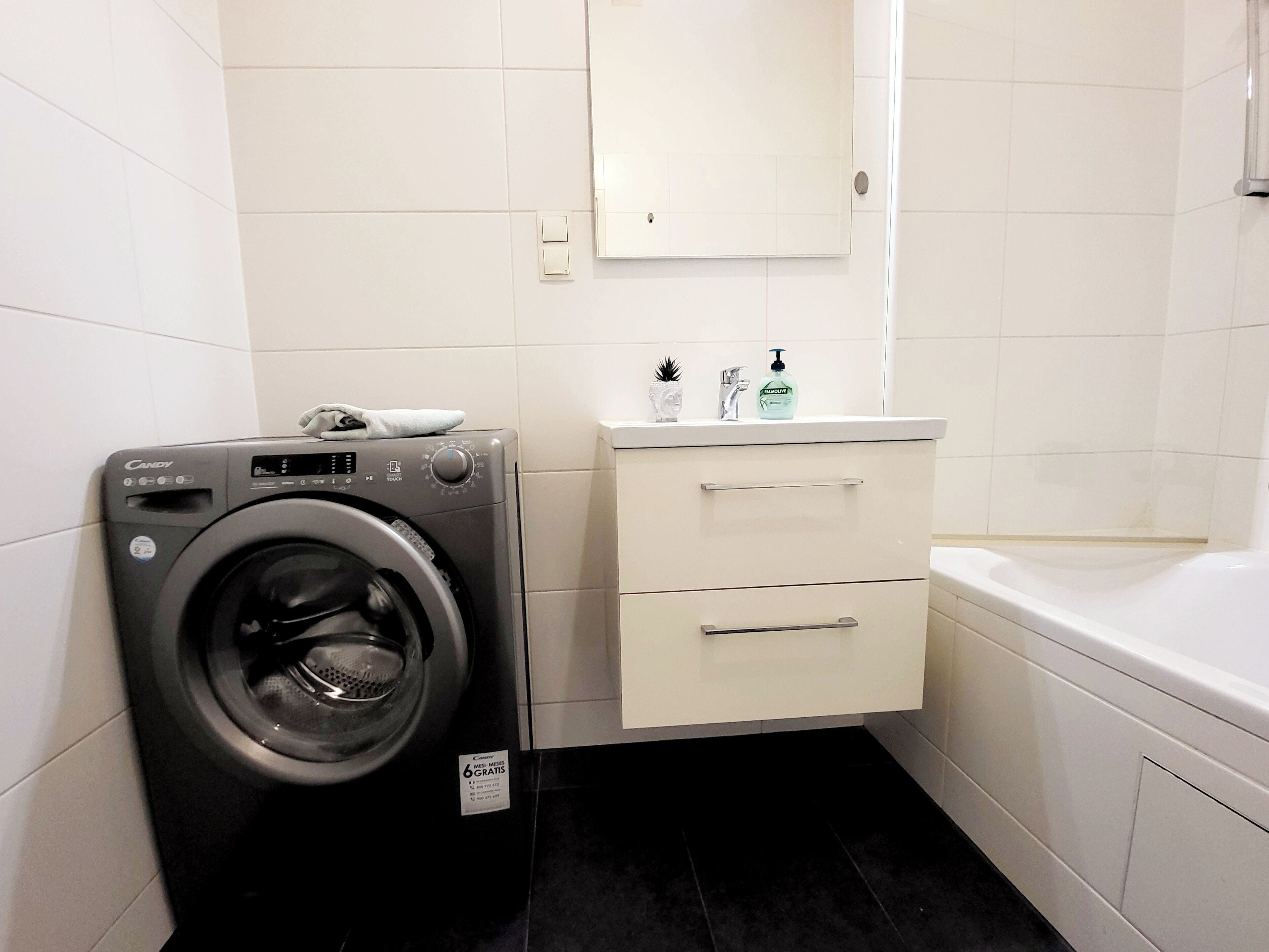A compact bathroom with a washing machine, a sink with toiletries, and a bathtub.