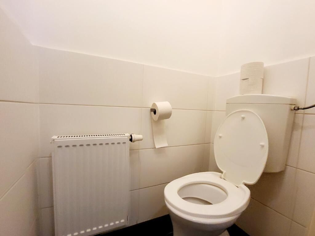 A bathroom with a toilet, a paper towel dispenser, and a radiator.