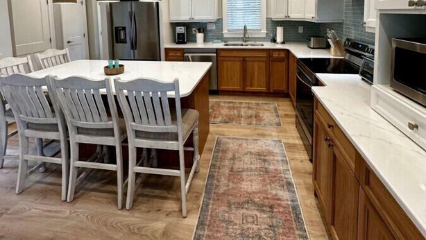 Una cocina moderna con armarios blancos, una isla central con asientos y un ventanal grande.