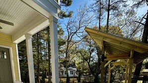 Un área de patio techada con mobiliario exterior, una pérgola y vistas de una casa al fondo.