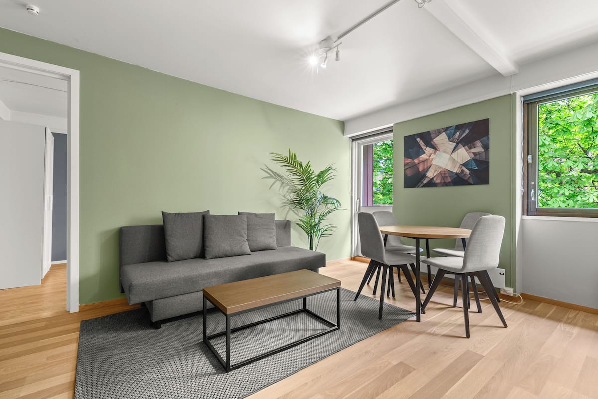 A modern living room with a grey sofa, a wooden coffee table, and a dining area with chairs and a table.