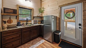 A kitchen with wooden cabinets, a stainless steel refrigerator, a microwave, and a window with blinds. - Cozy New Cabin I King Bed I Hot Tub I Fire Pit I Fast WiFi (Sevierville)