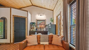 A cozy living room with a leather sofa, wooden flooring, and a kitchen area in the background. - Cozy New Cabin I King Bed I Hot Tub I Fire Pit I Fast WiFi (Sevierville)