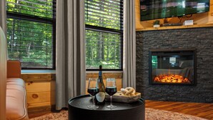 A cozy living room with a fireplace, a television mounted on the wall, and a window with blinds. - Cozy New Cabin I King Bed I Hot Tub I Fire Pit I Fast WiFi (Sevierville)