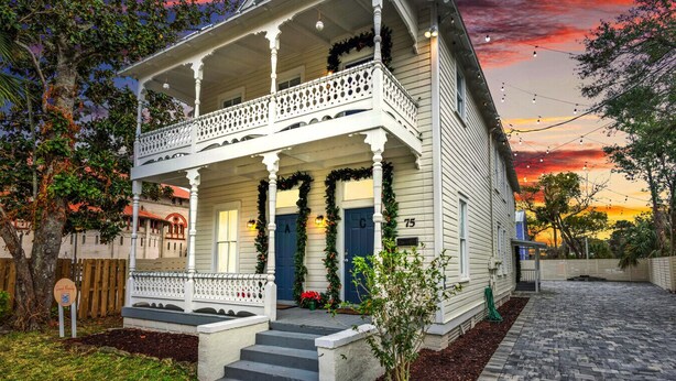 A white two-story house with a porch, a blue door, and a number '75' on the side.