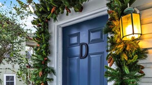A blue door with a 'D' monogram, surrounded by a wreath with pine branches and cones, and a lit lantern on the right. - Cedar Street Retreat - Unit D (St. Augustine)