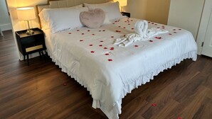 A neatly made bed with white linens, a heart-shaped pillow, and rose petals scattered across the bed. - Cedar Street Retreat - Unit D (St. Augustine)