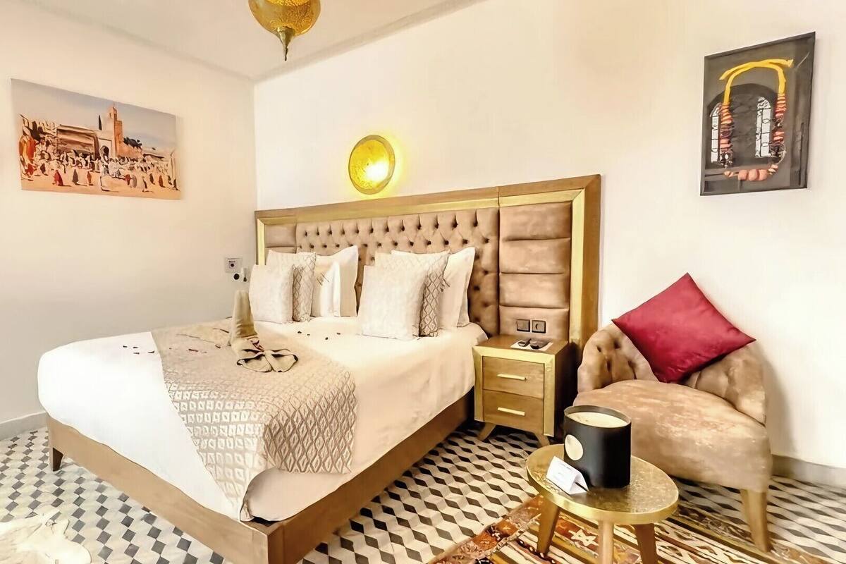 Hotellihuone, jossa on sänky, tuoli, yöpöytä, lamppu ja taideteoksia seinillä.