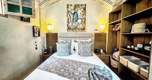 A hotel room with a large bed, two bedside tables, a headboard with a painting, a wardrobe, and a shelf with toiletries. - RIAD LUXE LOCATION - LE GRIZZLY (Marrakech)