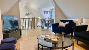 Ein modernes Wohnzimmer mit Fernseher, Sitzgelegenheiten und einem Essbereich im Hintergrund.