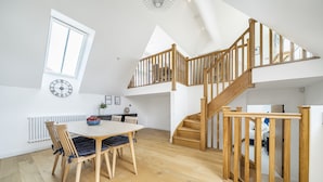 Ein geräumiger Raum mit einer Holztreppe, einem Essbereich mit Tisch und Stühlen sowie einem großen Fenster.