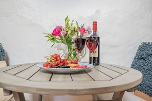 Et rundt træbord med en tallerken druer, et glas rødvin og en vase blomster.