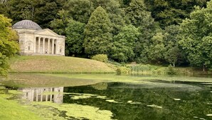 A classical building with columns and a dome, surrounded by lush greenery and a calm pond. - Dovehayes Cottage  - Bourton, Shaftesbury (Gillingham)