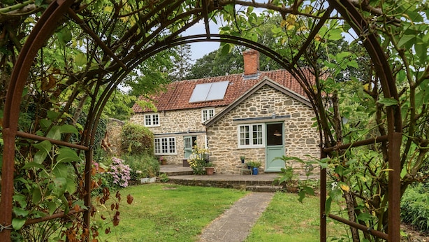 A stone house with a red-tiled roof, a green door, and a pathway leading to the entrance. - Dovehayes Cottage  - Bourton, Shaftesbury (Gillingham)