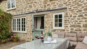 A stone building with a glass table, two windows, and a green door. - Dovehayes Cottage  - Bourton, Shaftesbury (Gillingham)