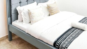 Un dormitorio con cabecera tapizada en gris, ropa de cama blanca y una lámpara colgante.