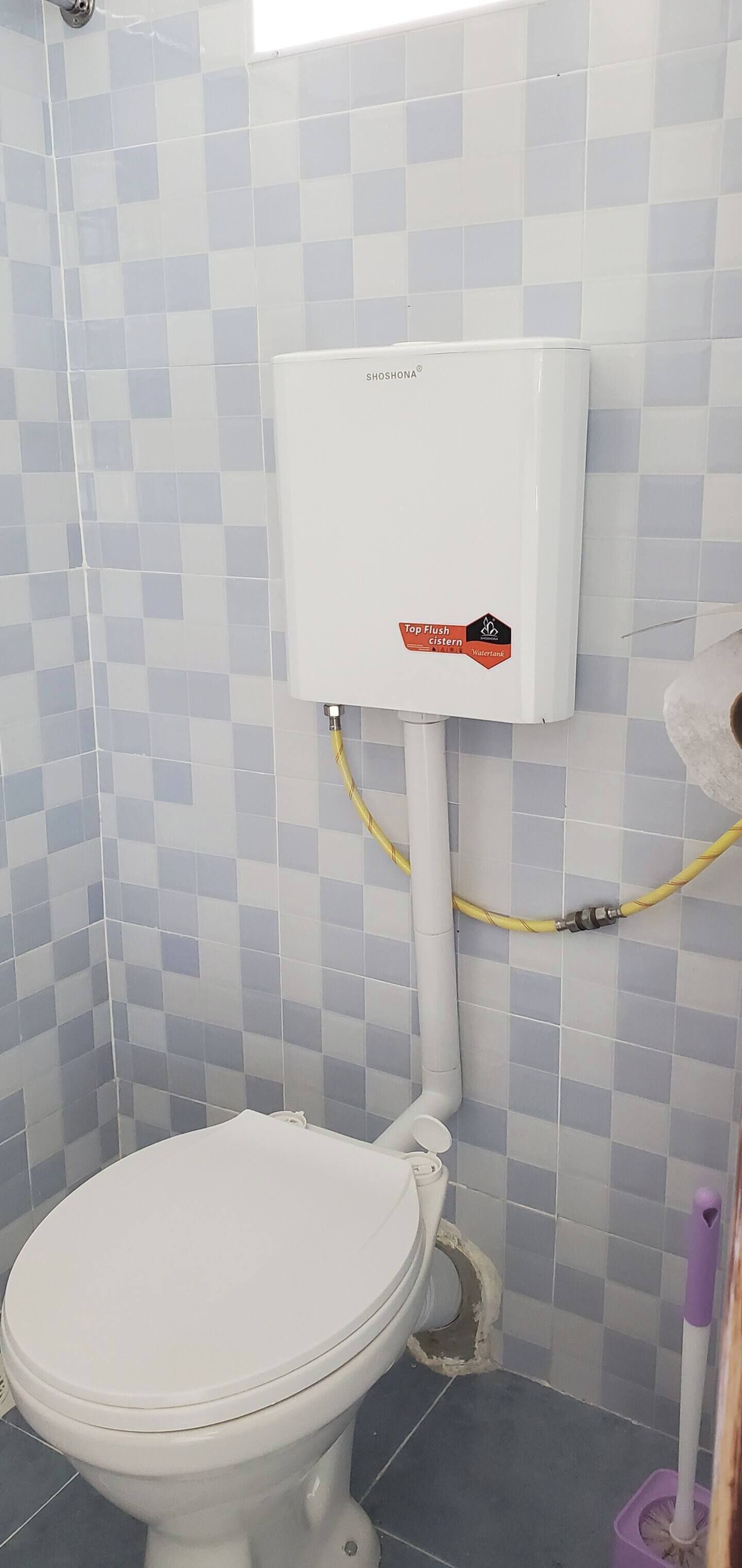 A bathroom with a toilet, a water heater, and a mop.