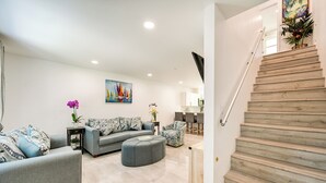 Ein modernes Wohnzimmer mit einem grauen Sofa, einem passenden Hocker und einem Bild von Segelbooten an der Wand.