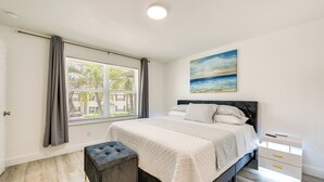 Ein Schlafzimmer mit einem Bett, einem Fenster mit Vorhängen, einem Nachttisch und einem Bild an der Wand.