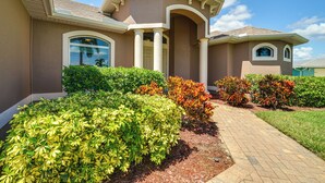 A modern house with a brick pathway leading to the entrance, surrounded by well-maintained shrubs and a clear sky. - Cape Coral Villa: Heated Pool & Gulf Access! (Cape Coral)