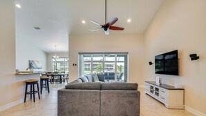 A spacious living area with a gray sectional sofa, a ceiling fan, a flat-screen TV, and a dining area with chairs and a table. - Cape Coral Villa: Heated Pool & Gulf Access! (Cape Coral)