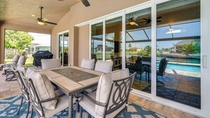 A patio area with a table and chairs, a ceiling fan, and a view of a swimming pool through glass doors. - Cape Coral Villa: Heated Pool & Gulf Access! (Cape Coral)
