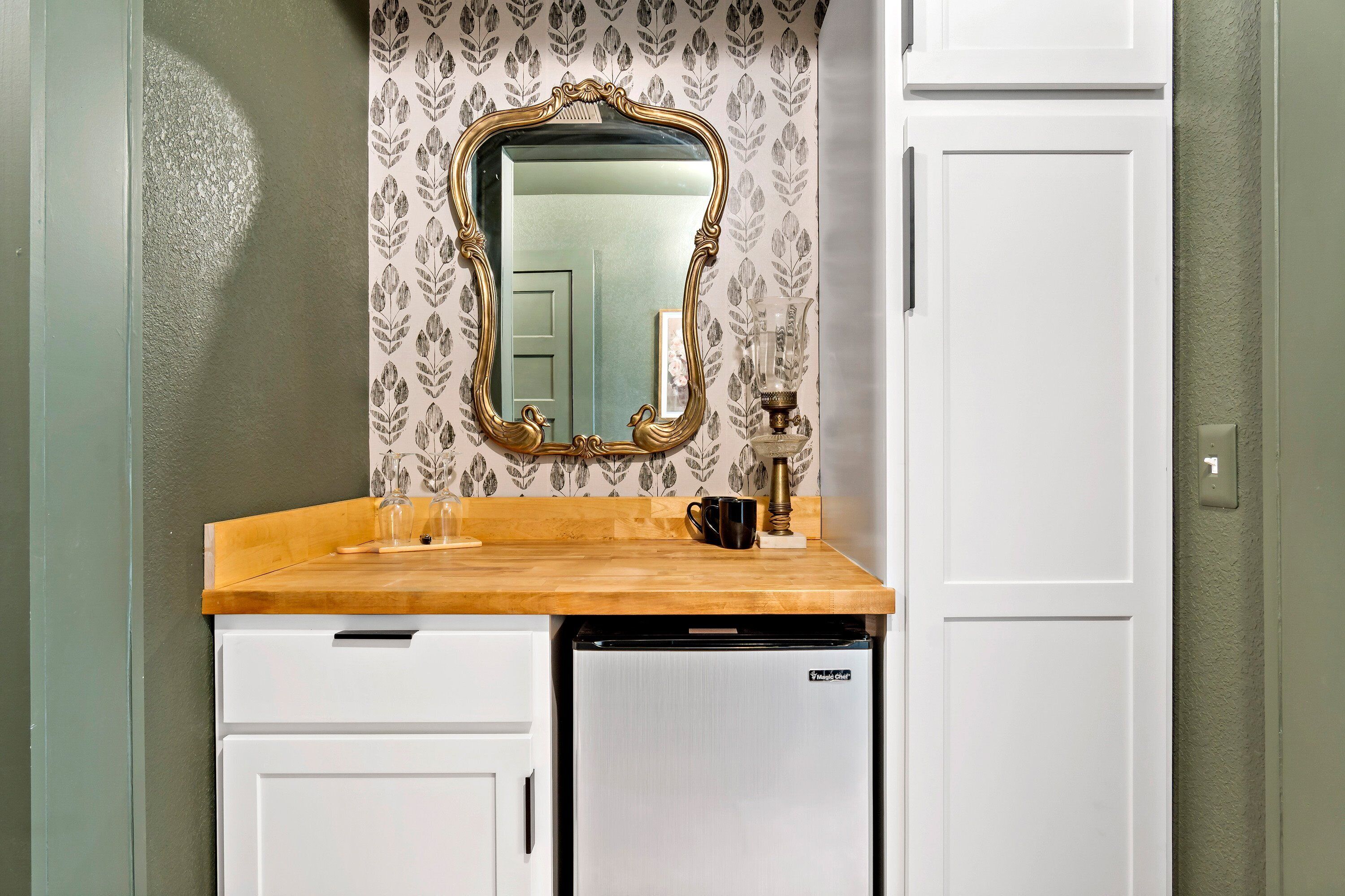 A bathroom with a wooden countertop, a white sink, a mirror with an ornate frame, a white cabinet, and a refrigerator.
