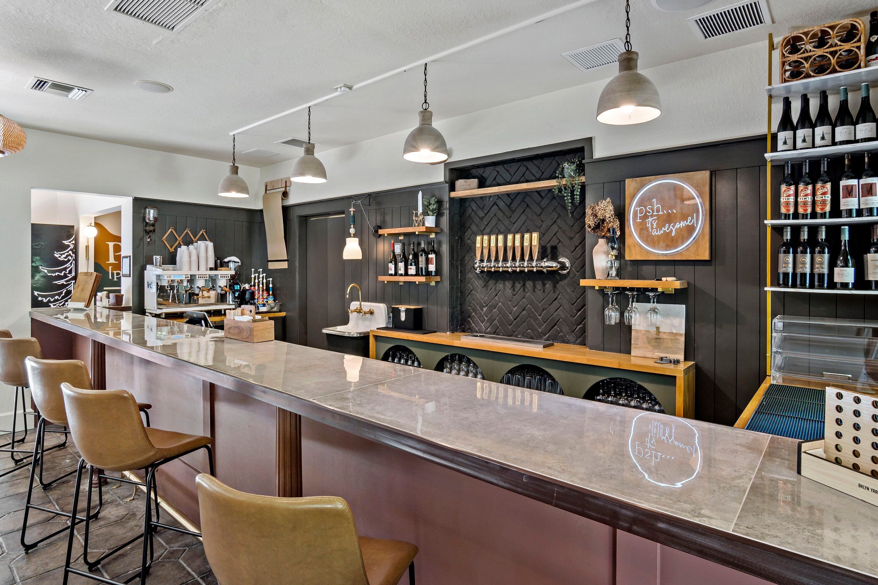 Un espace bar doté d’un long comptoir, de tabourets et d’étagères remplies de bouteilles.