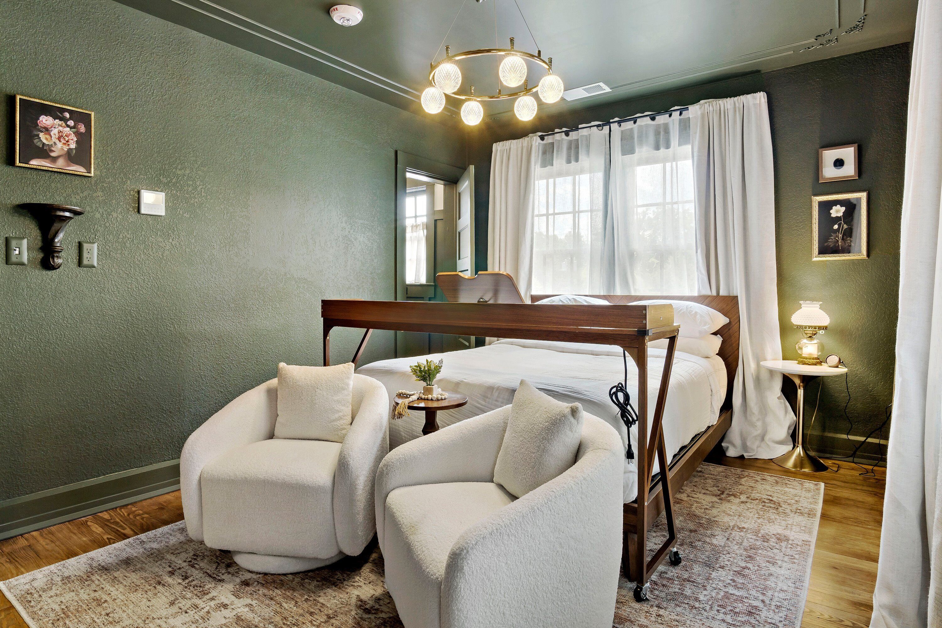 Une chambre avec un lit superposé, deux fauteuils, une table de chevet avec une lampe et une grande fenêtre avec des rideaux.