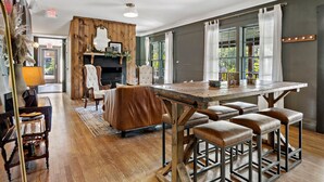 A spacious dining area with a wooden table and leather stools, a fireplace, and large windows with curtains. - Peri Social House (Black Mountain)