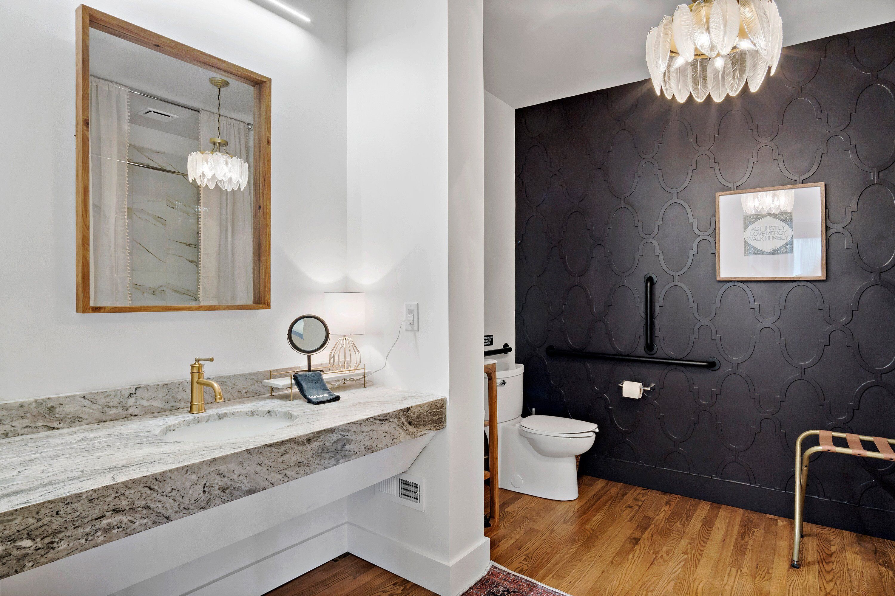 Une salle de bain avec un lavabo en marbre, un robinet doré et un miroir encadré en bois. On y trouve également des toilettes, un porte-serviettes noir et un tableau encadré accroché au mur.