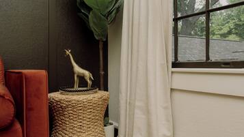 A room with a woven stool, a giraffe figurine, a red chair, and a window with a view of trees.